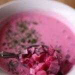 Close-up of a bowl of vibrant pink beetroot soup with parsley garnish and a spoonful of diced beets.
