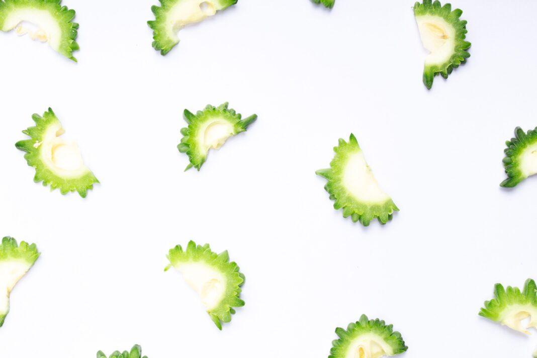 Green bitter melon slices arranged on a white surface, showcasing vibrant texture and color.