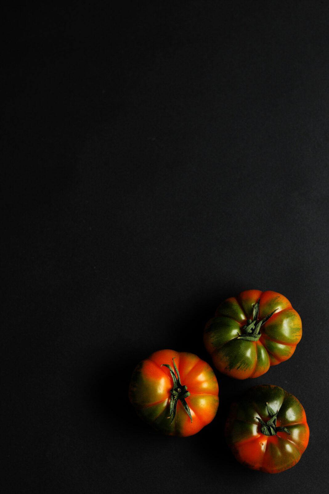 Three organic tomatoes arranged on a black background with dramatic lighting.