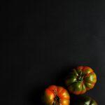 Tomates noires bienfaits et meilleures variétés pour serres et plein air Three organic tomatoes arranged on a black background with dramatic lighting.