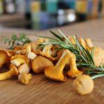 Girolles: si elles netaient pas là hier, elles apparaissent en une nuit Close-up of fresh chanterelle mushrooms and rosemary sprigs on a wooden table, ideal for cooking.