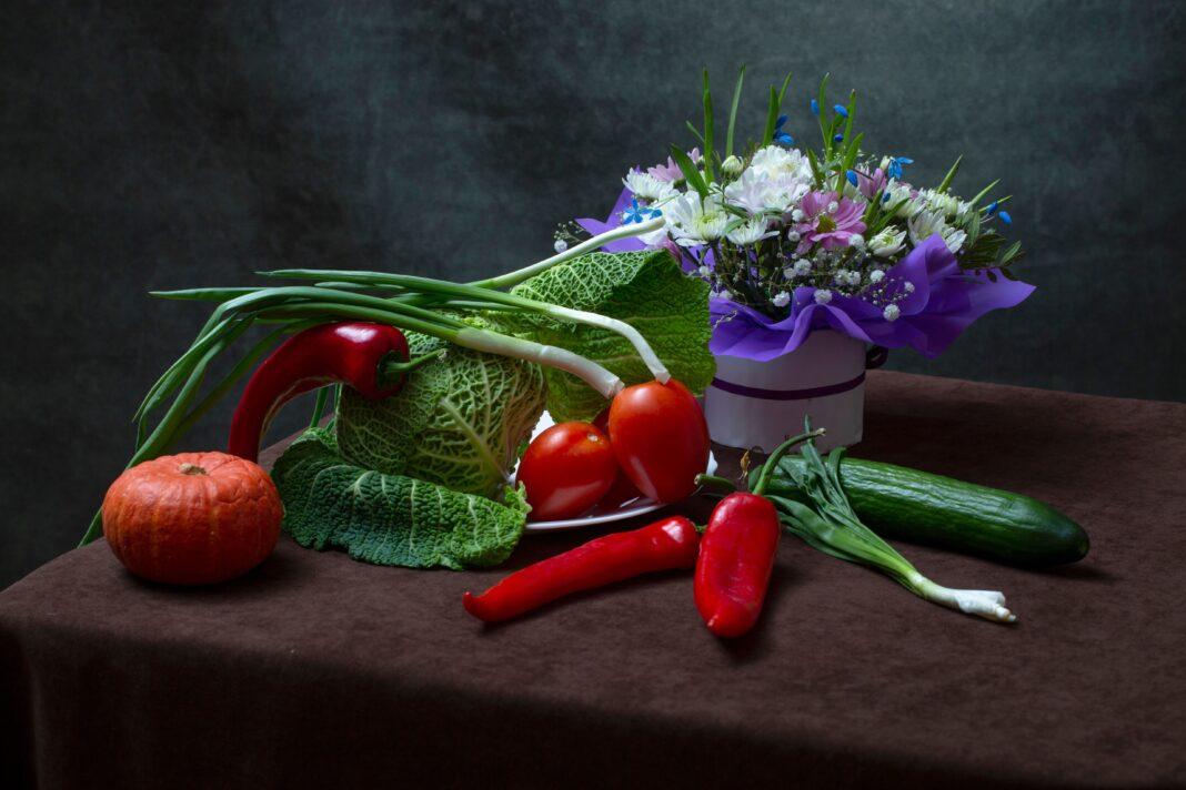 A colorful arrangement of vegetables and a flower bouquet on a table.