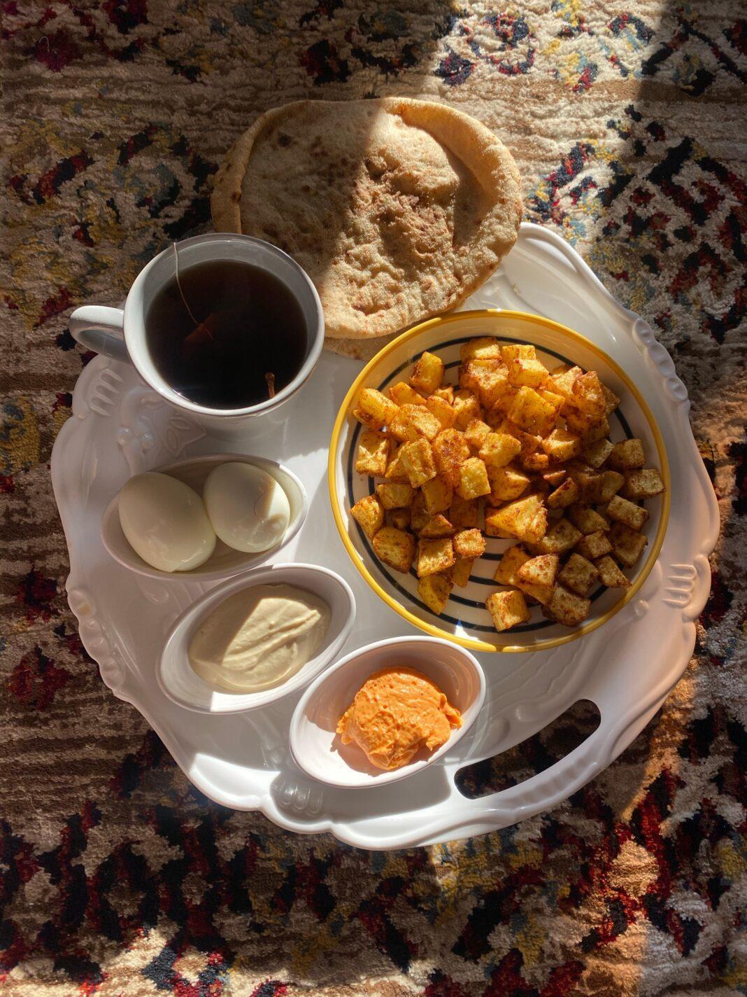 A cozy breakfast set with tea, potatoes, bread, and eggs in morning light.