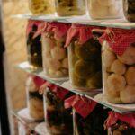 Conserves de tiges dail en hiver recettes simples et savoureuses Homemade pickled vegetables in jars with red cloth caps on rustic shelves.