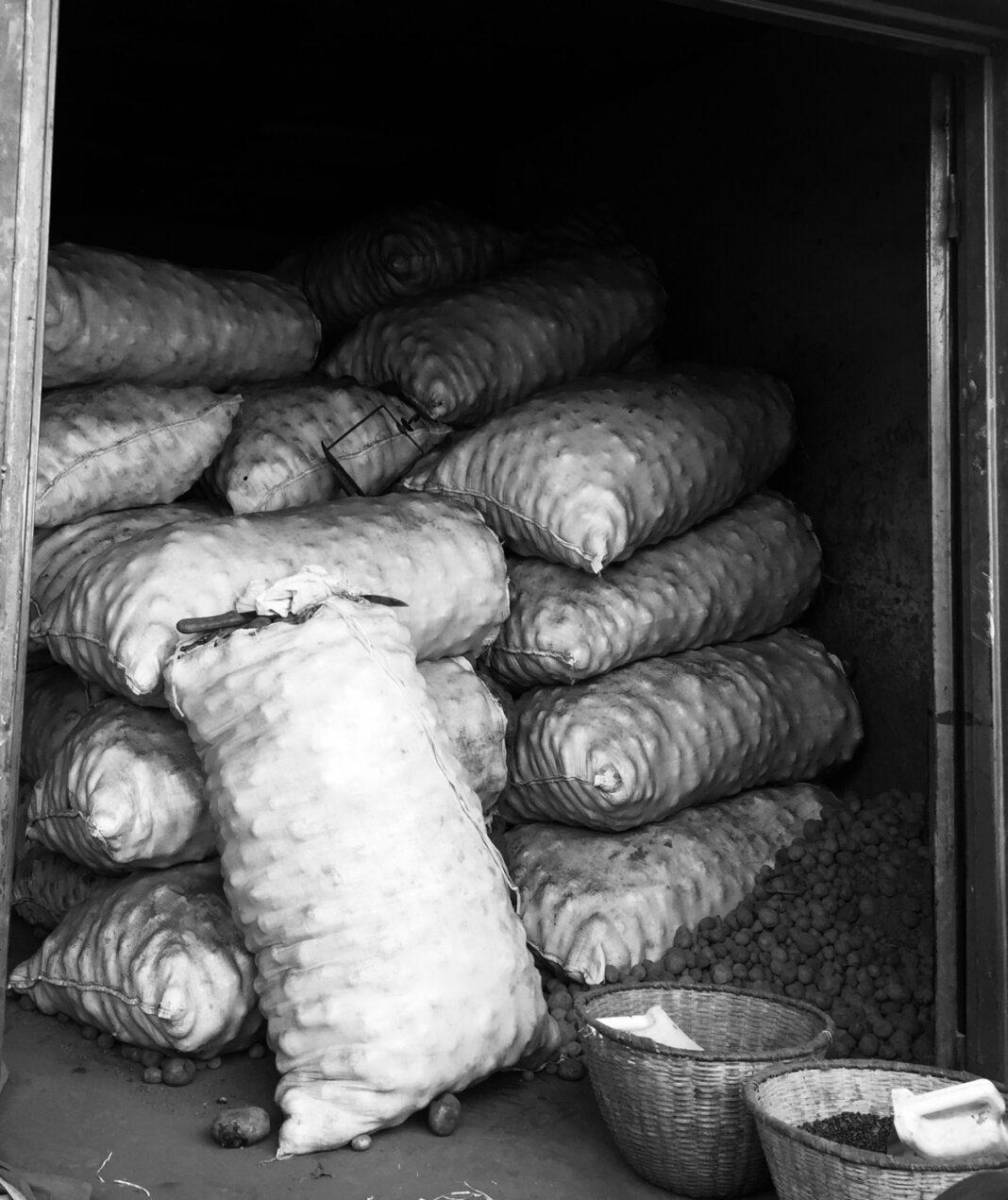 Black and white image of potato sacks stacked in a warehouse, showcasing industrial storage.