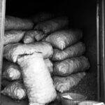 Black and white image of potato sacks stacked in a warehouse, showcasing industrial storage.