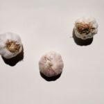 Planter lail dhiver en septembre Quand comment et pourquoi Artistic top view shot of three garlic bulbs against a light background, highlighting their textures.
