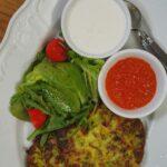Meilleures recettes de caviar de courgettes pour l'hiver en boîte A tasty zucchini fritter served with fresh salad and two distinct sauces on a white plate.
