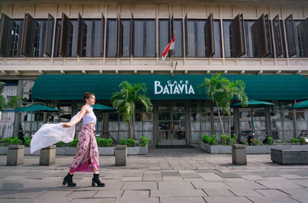A fashionable woman walks past Café Batavia in Jakarta, Indonesia, showcasing modern urban lifestyle.