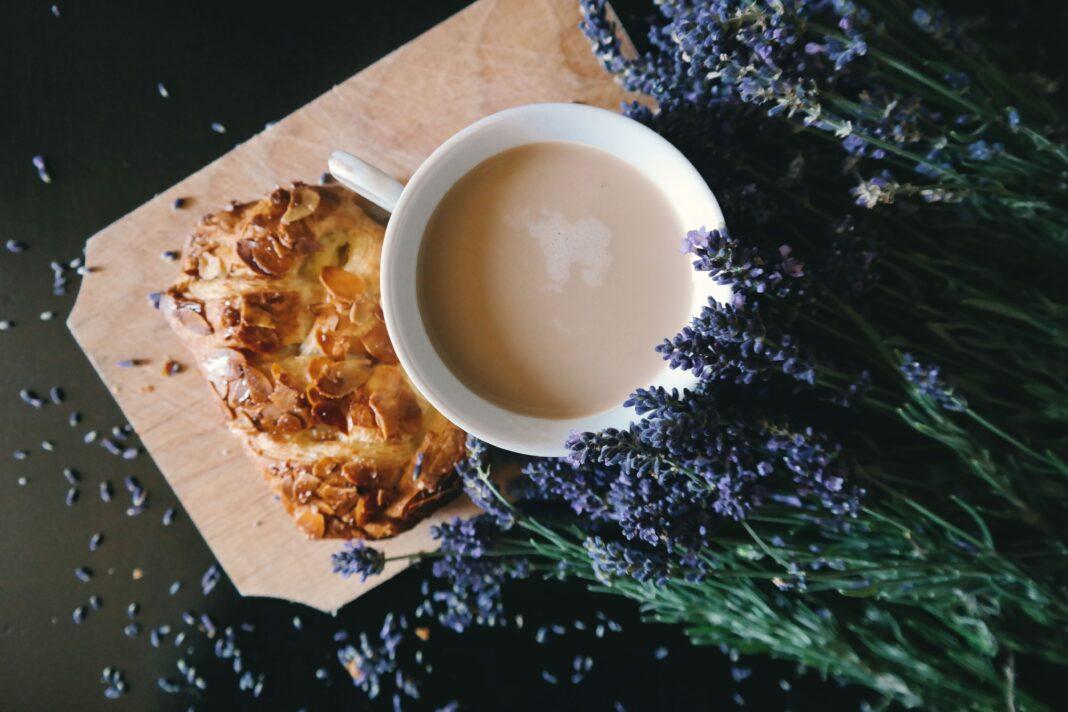 A cup of coffee and pastry on a wooden board surrounded by lavender flowers.