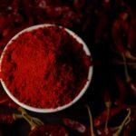 Vibrant chili powder in a bowl surrounded by dried red chilies, perfect for spice lovers.