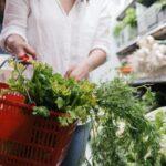 Sauver son persil de supermarché : les gestes qui changent tout A person holding a grocery basket filled with fresh greens like celery and parsley in a store.