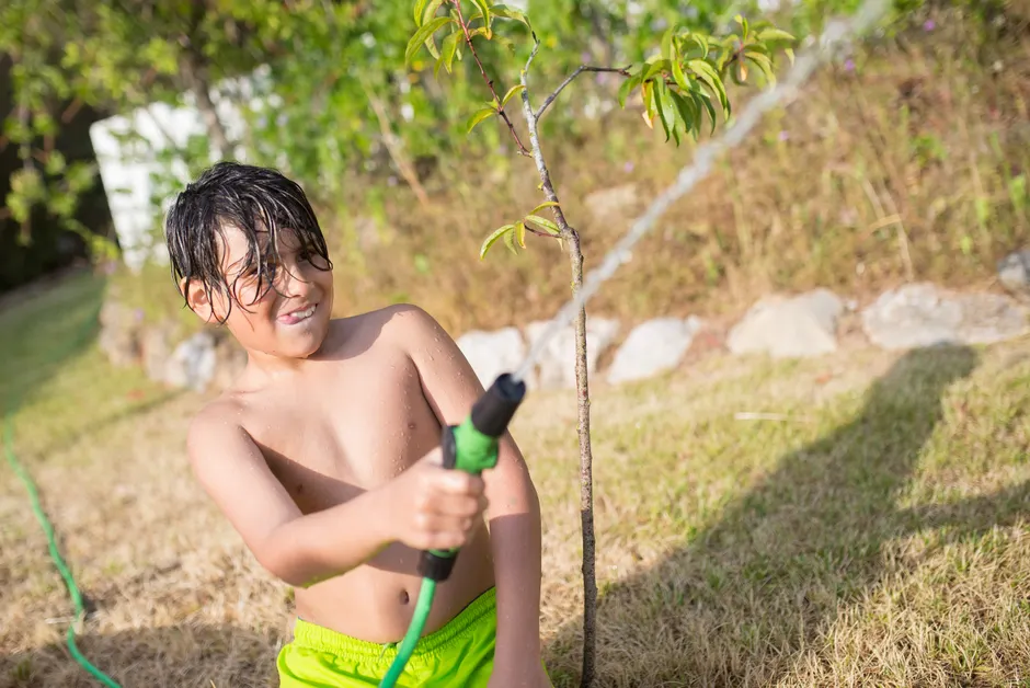 A cheerful child enjoys a sunny afternoon watering plants with a hose in a garden.