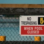 Piscine au jardin en 2026 : 4 protections, zéro improvisation A 'No Trespassing' sign on a chain link fence at a closed swimming pool, ensuring safety and security.