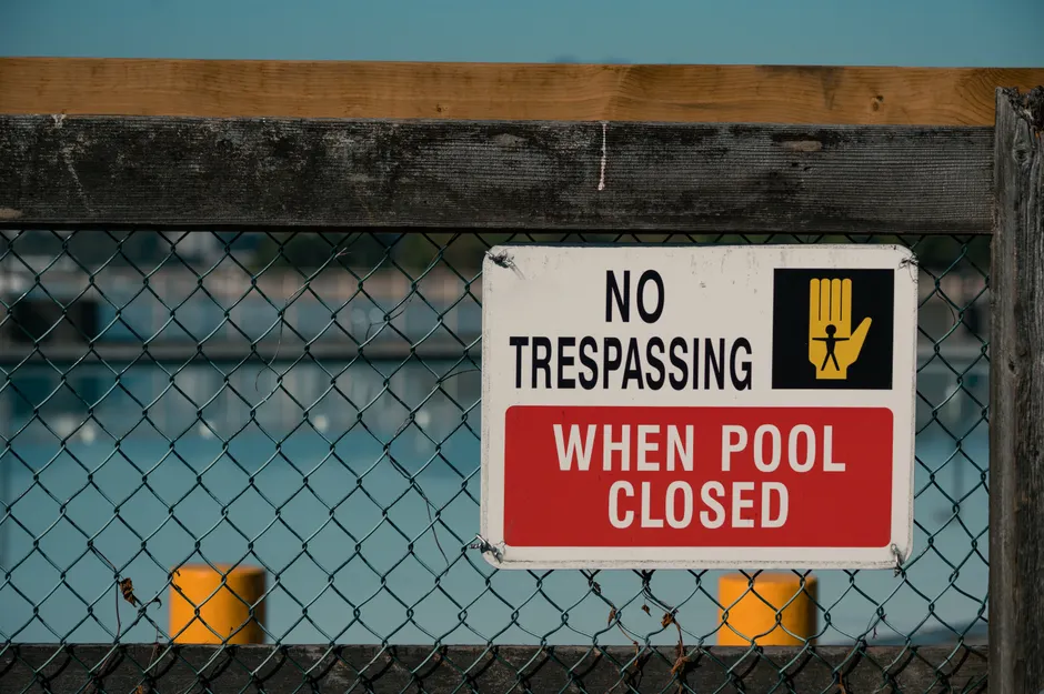 A 'No Trespassing' sign on a chain link fence at a closed swimming pool, ensuring safety and security.