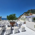 Bright sunny terrace overlooking the Mediterranean with white furniture and coastal views.