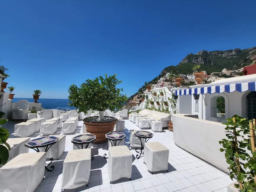 Bright sunny terrace overlooking the Mediterranean with white furniture and coastal views.