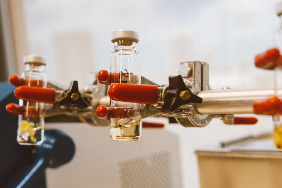 Detailed view of laboratory glass vials held by a clamp with red handles, ideal for science stock images.