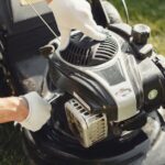 Tondeuse en panne : réparer ou remplacer avant la première tonte? Hands in gloves adjusting a lawn mower outdoors, perfect for gardening themes.