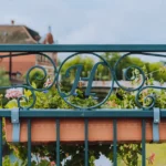 Jardinière fleurie en été : 3 règles et un piège A close-up of a decorative iron fence with flowers in a flower box and a lock.