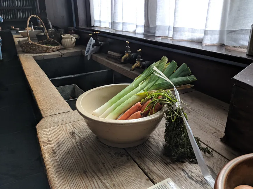 A cozy kitchen scene with a bowl of fresh vegetables including carrots and leeks by the window in Cornwall.