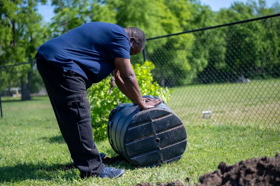 A man working with a compost bin in a sunny park, promoting outdoor gardening activities.