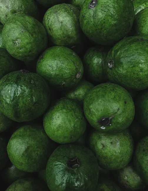 A stack of fresh green feijoas showcasing abundance and vibrant color in a vertical shot.