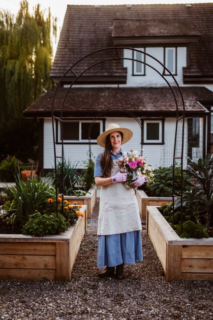 A woman in a sun hat stands in a garden, holding a bouquet of colorful flowers.