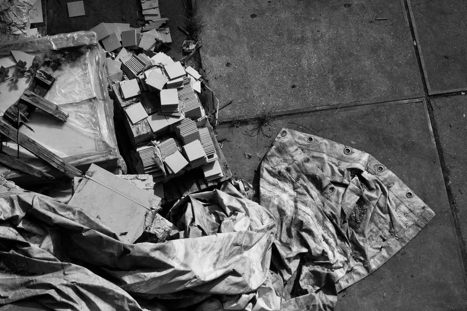 Black and white photo of a worn-out tarp and building materials at an abandoned site.