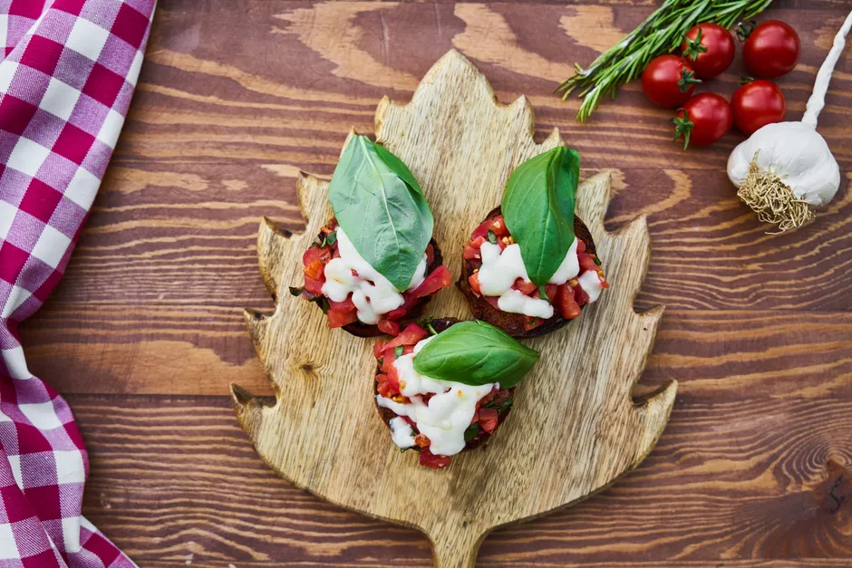 Delicious homemade bruschetta topped with fresh basil, tomato, and cheese on a rustic wooden board.