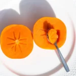 Kaki : croquez-le ou sortez la cuillère, d'octobre à janvier Fresh sliced persimmon on a white plate with a spoon. Perfect for healthy food themes.