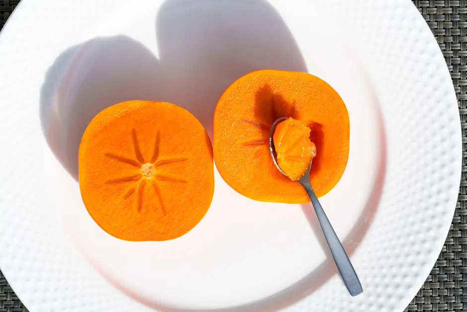 Fresh sliced persimmon on a white plate with a spoon. Perfect for healthy food themes.