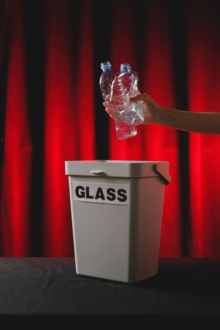 Hand placing plastic bottles into a glass bin against red background.