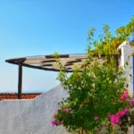 Mediterranean terrace with blue door, flowers, and sunny sky.