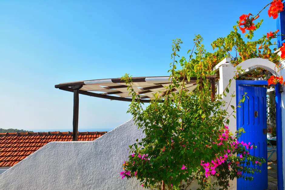 Mediterranean terrace with blue door, flowers, and sunny sky.
