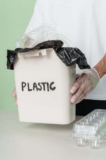Person handling a plastic recycling bin with gloves, highlighting waste management.