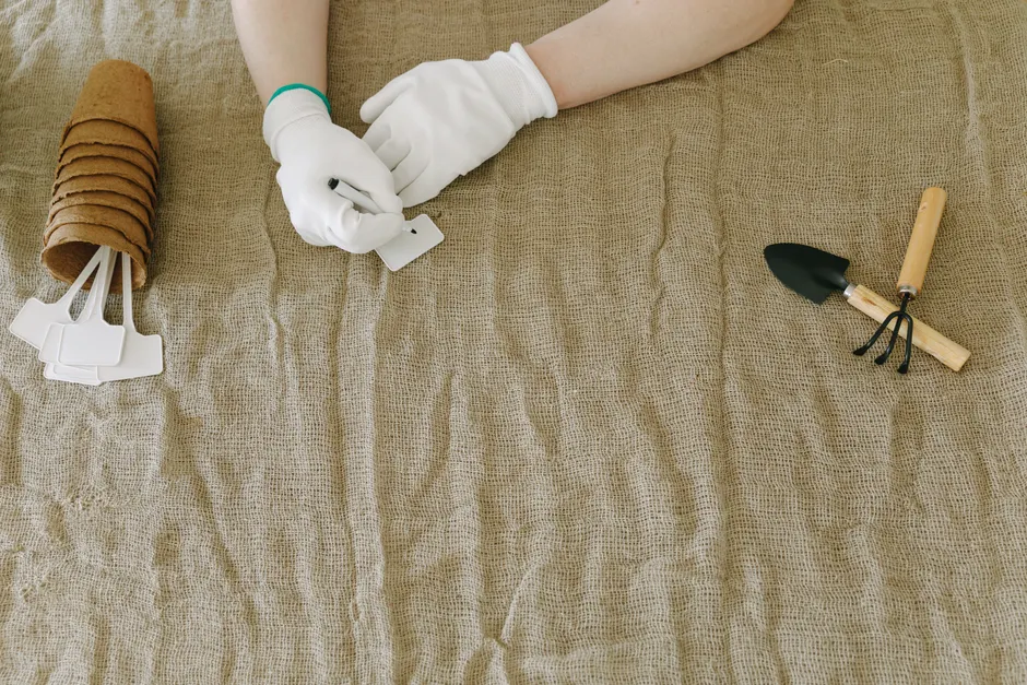 Person preparing gardening tools and labels on burlap surface, wearing gloves.