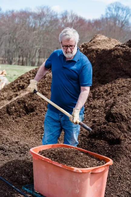 Senior man working outdoors with a shovel and compost. Engaging in sustainable farming practices.