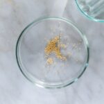 Top view of mustard seeds in a clear petri dish on a marble surface.