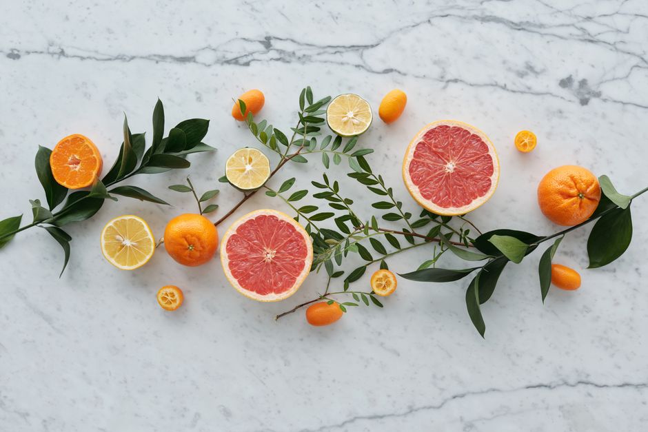 Vibrant citrus fruits including orange, grapefruit, and lemon arranged with green leaves on a marble surface.