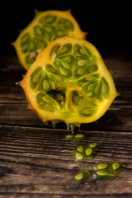 Vibrant kiwano fruit sliced open, displaying seeds and juicy interior on wooden surface.