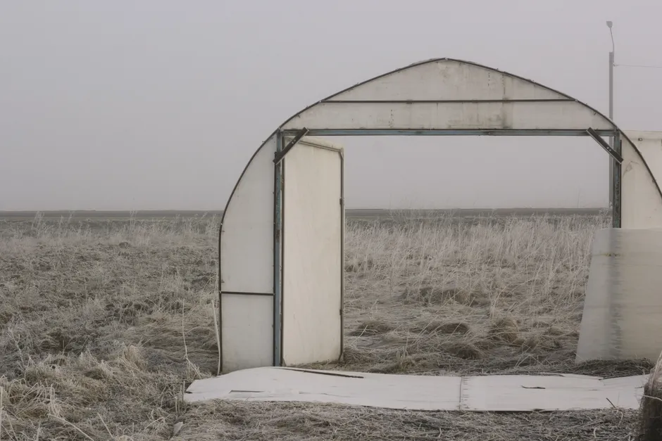A deserted metal door frame in a frosty field under a gray sky.