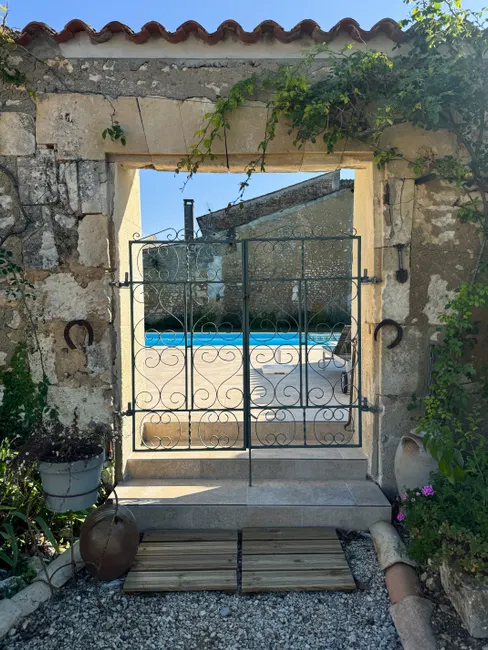 A picturesque stone entryway with wrought iron gate opening to a swimming pool in Pons, France.