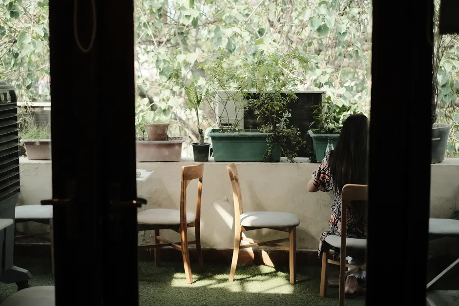 A serene balcony view featuring a woman sitting amidst potted plants and chairs.