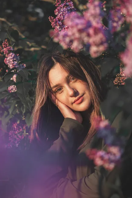A young woman surrounded by blooming lilacs in a serene garden setting on a sunny day.