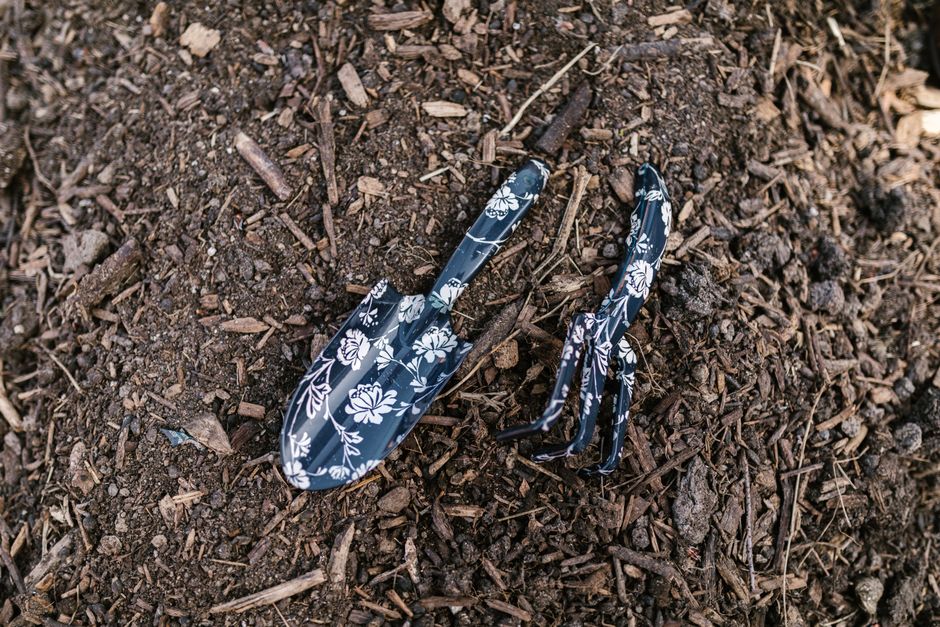 Close-up of floral patterned rake and shovel resting on soil, ideal for gardening themes.