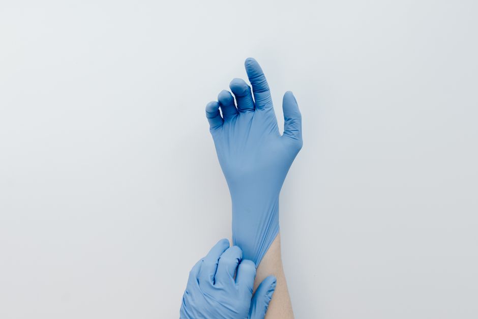 Close-up of hands putting on blue medical gloves against a white backdrop.