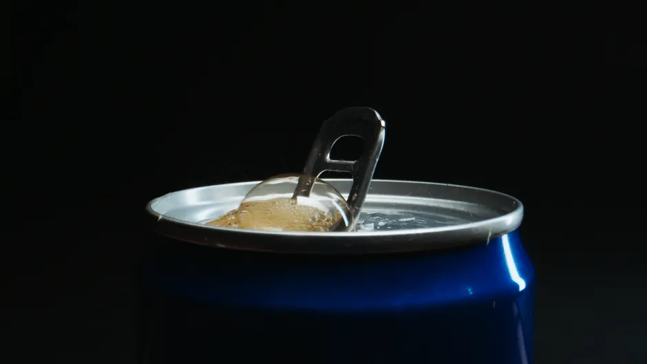 Detailed close-up of an open soda can with bubbles rising in a dark setting