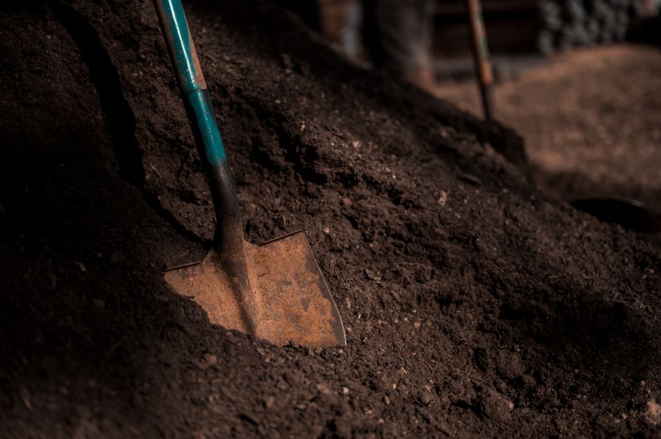 Shovel embedded in dark soil, showcasing texture and gardening tools.
