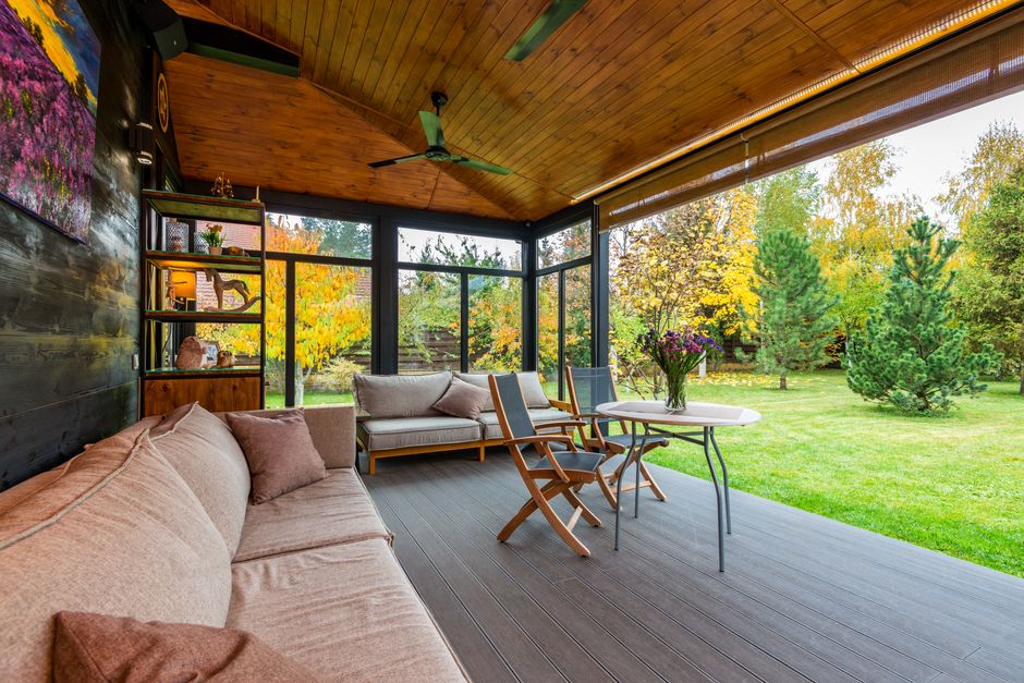 Sofas placed near wooden wall decorated with picture veranda furnished with armchairs near table under fan on ceiling